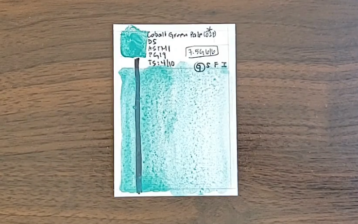 A swatch of Cobalt Green Pale, a granulating light-valued blue-green paint, by Daniel Smith sits on a wood table.