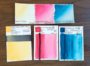 Swatches of Naples Yellow (a light, creamy yellow), Quinacridone Rose (a vibrant magenta), and Ultramarine Turquoise (a vibrant blue-green) sit on a wood table.